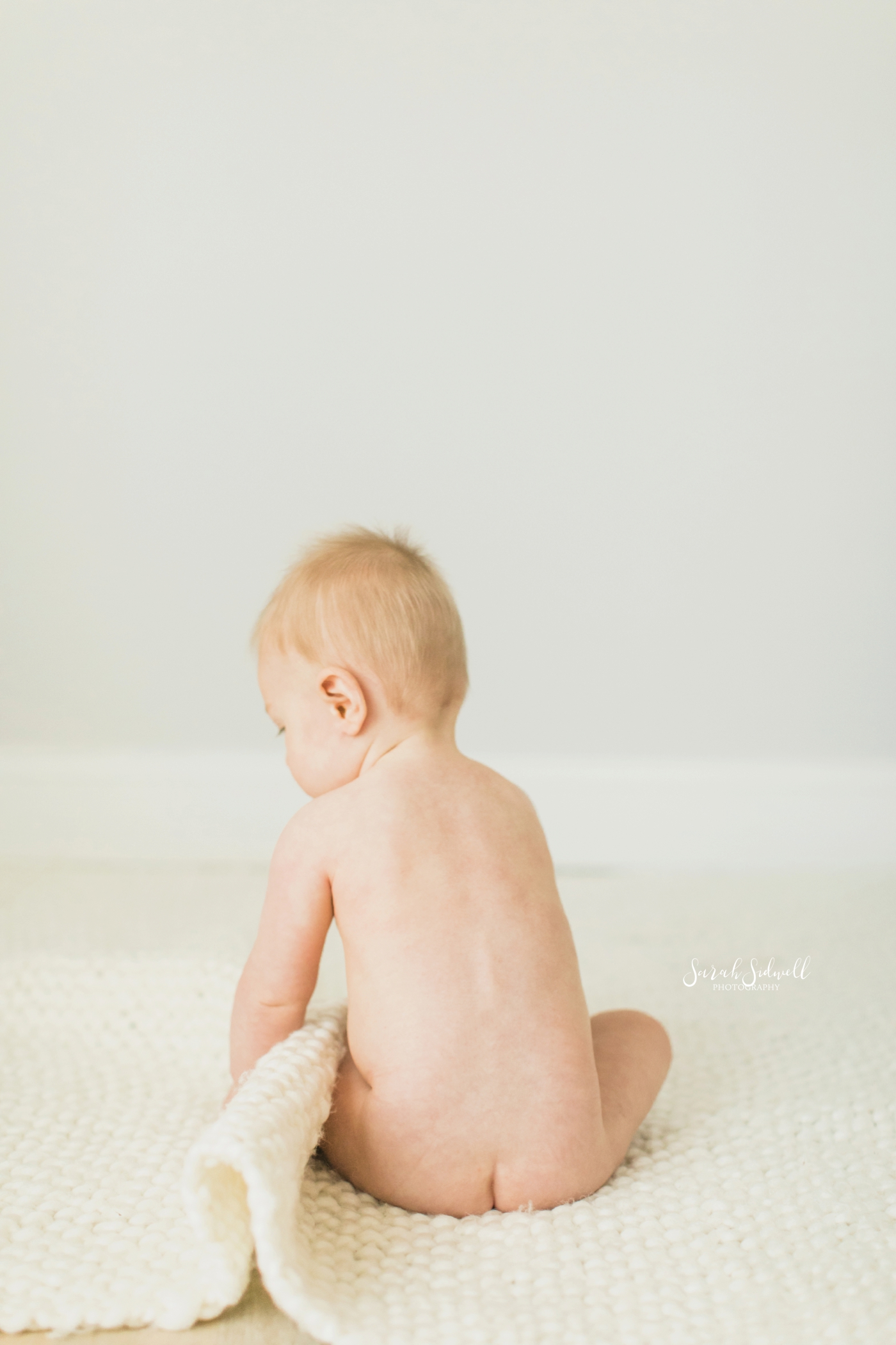 A baby sits on the floor with his bottom showing. 