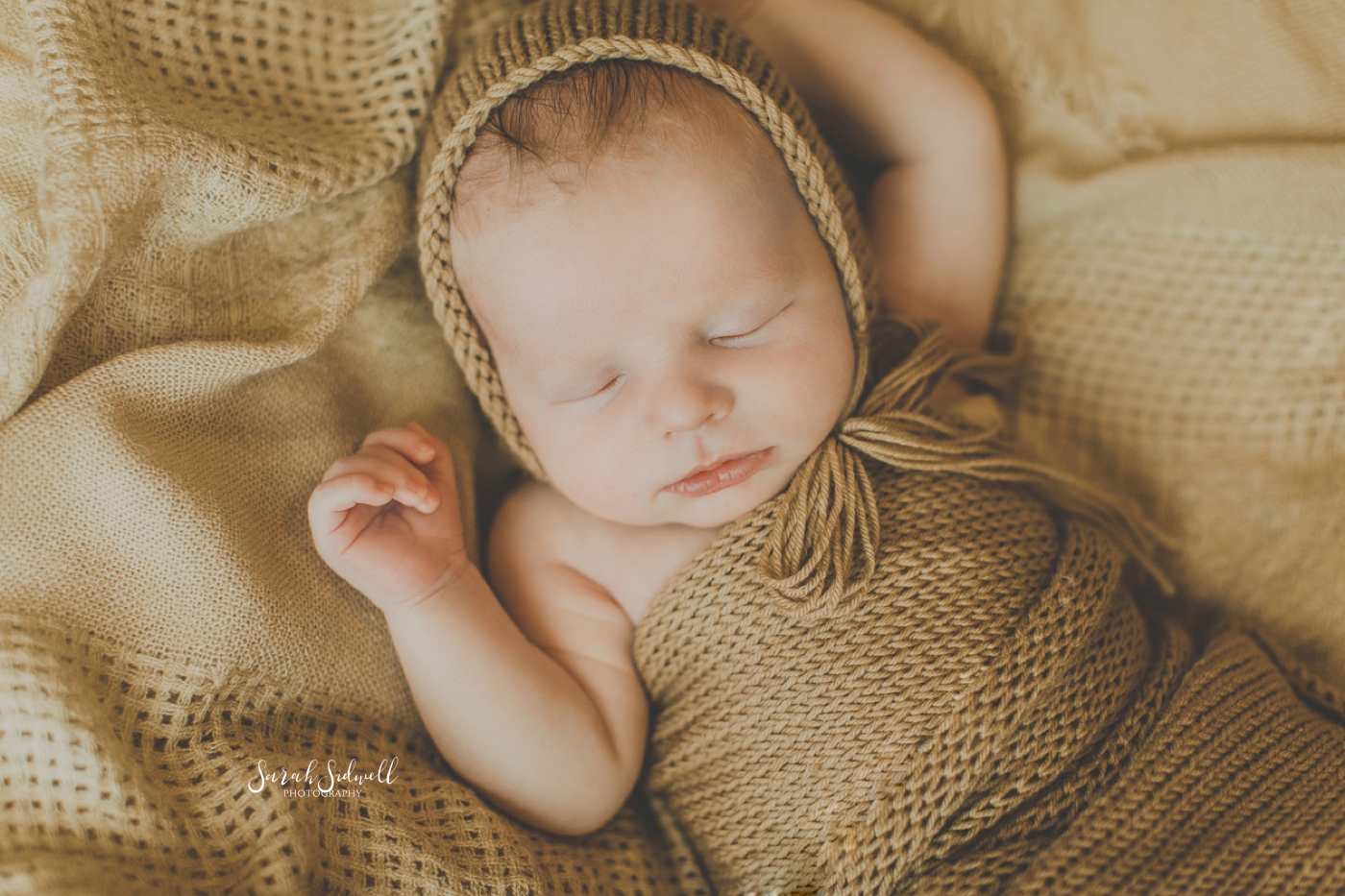 A newborn sleeps in a bonnet. 