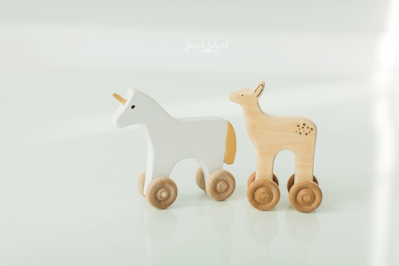 Wooden toy horse are displayed on a floor. 