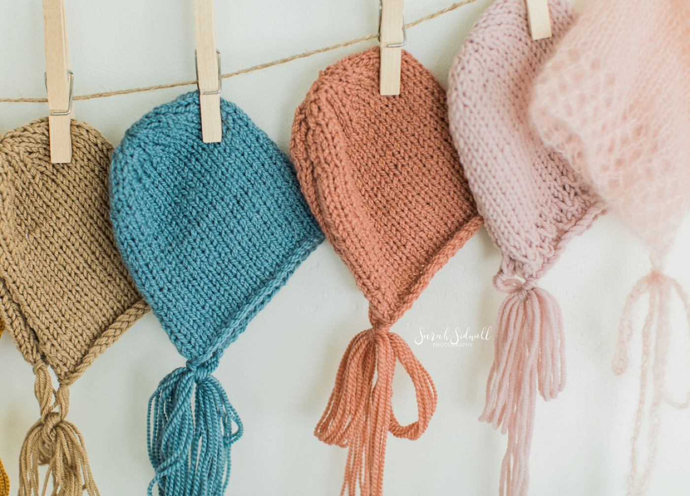 Knitted baby hats are pinned to a clothes line. 