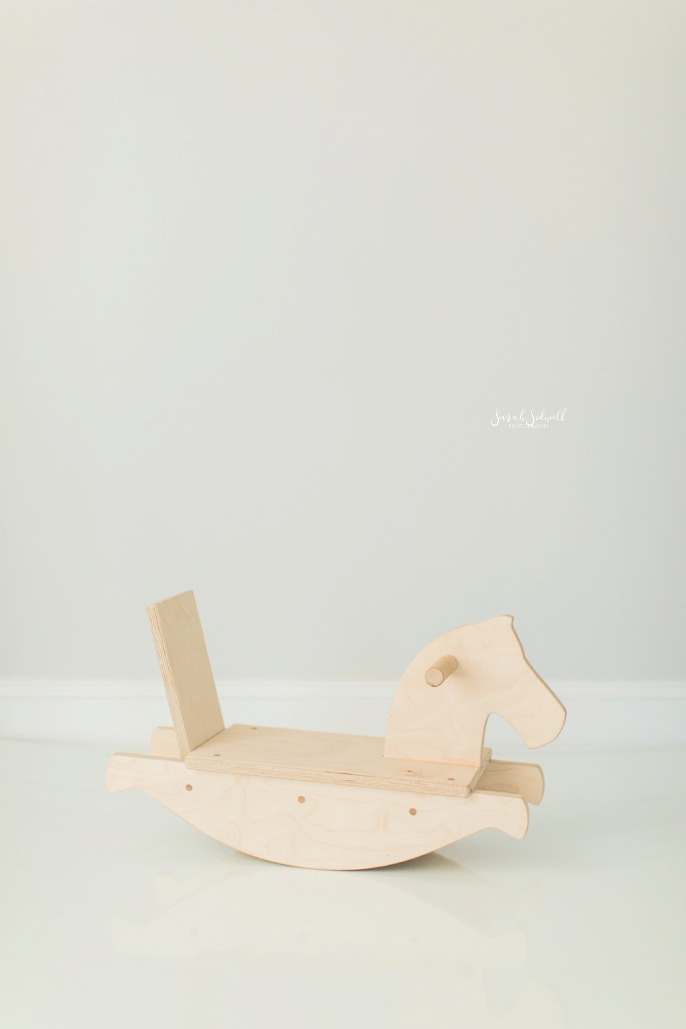 A wooden rocking horse is sitting in a white room. 