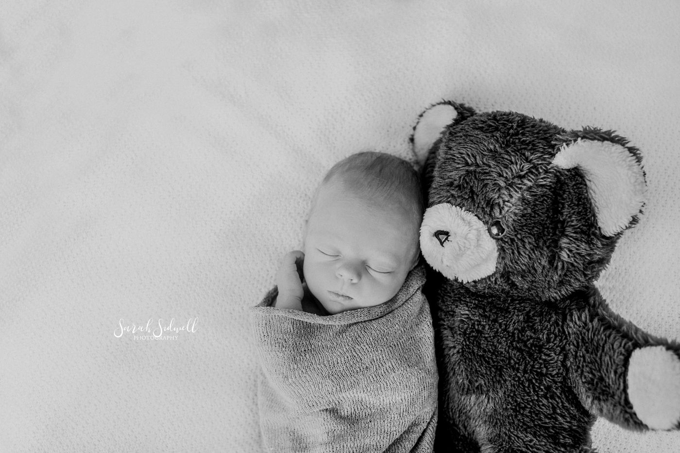 A baby sleeps next to a teddy bear. 