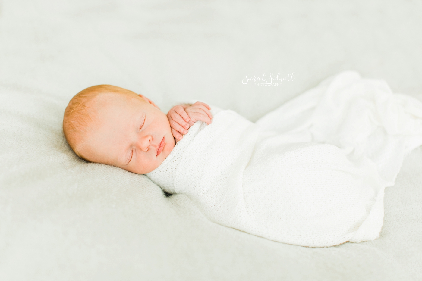 A baby sleeps swaddled in a white blanket. 