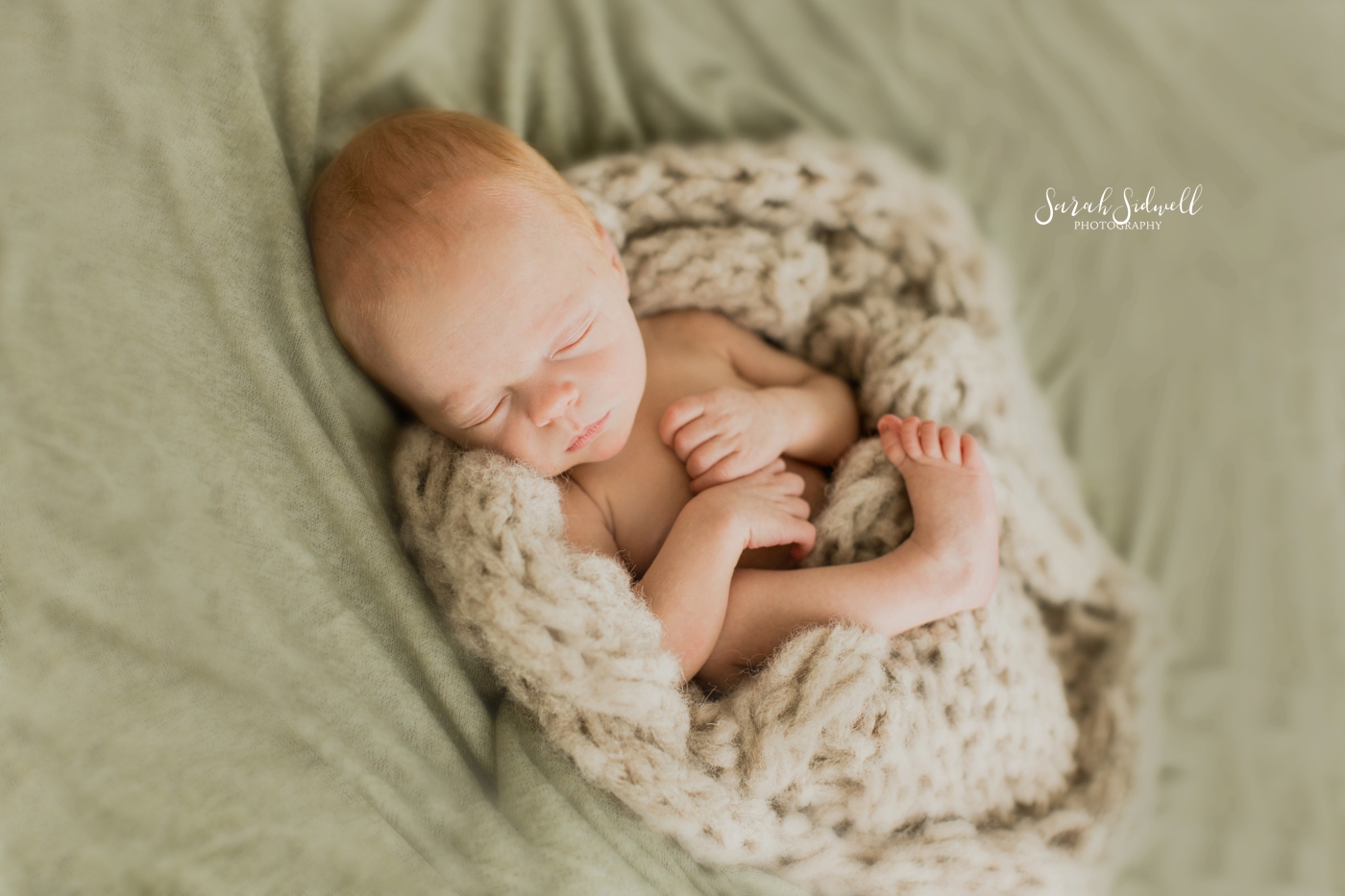 A baby sleeps wrapped in a knitted blanket. 