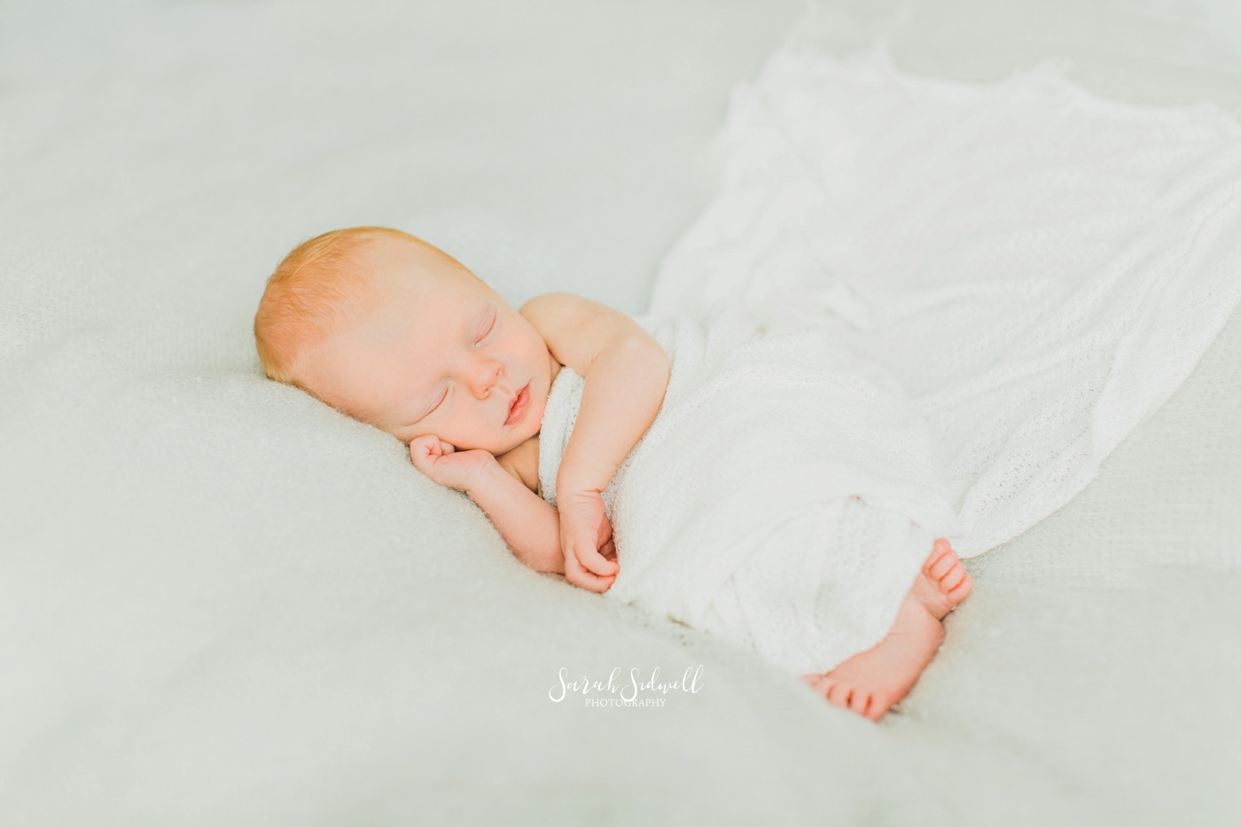 A baby sleeps under a white blanket. 