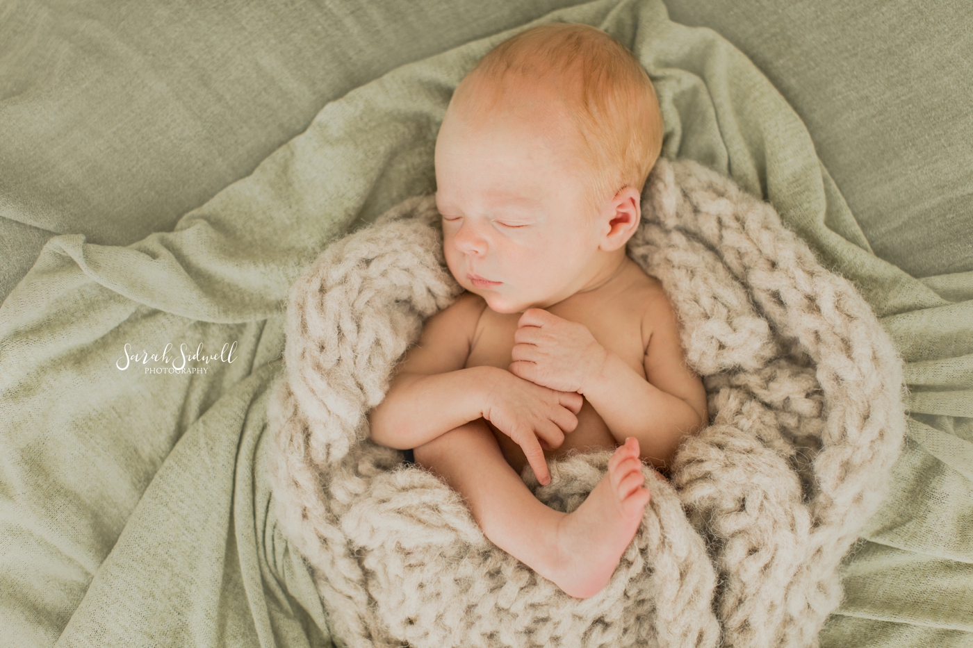 A baby sleeps curled up under a soft blanket. 