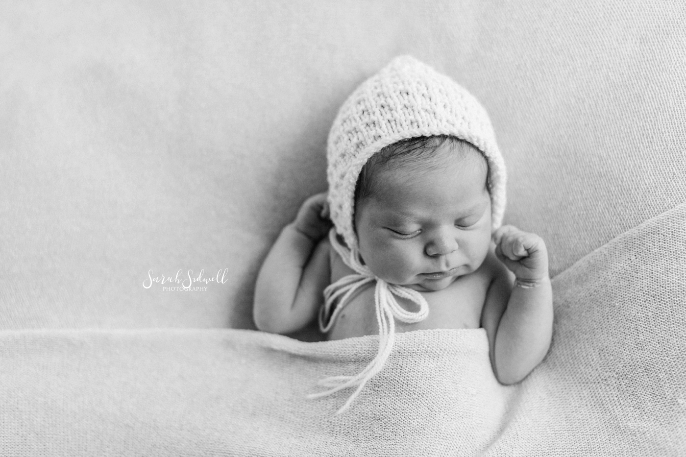 A baby wears a white bonnet. 