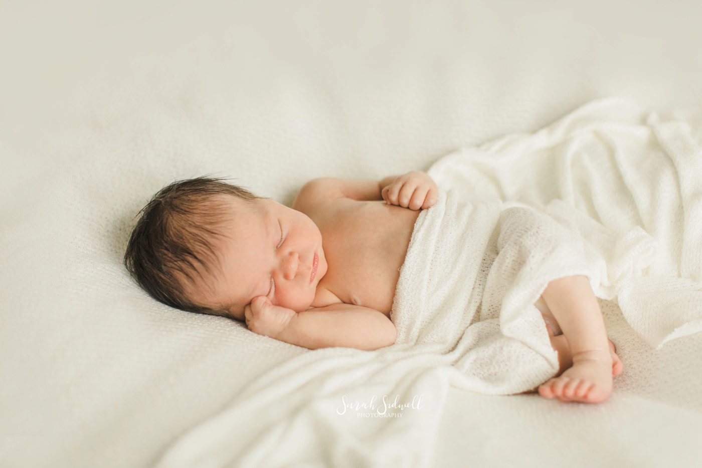 A baby sleeps with a white blanket on top of her. 