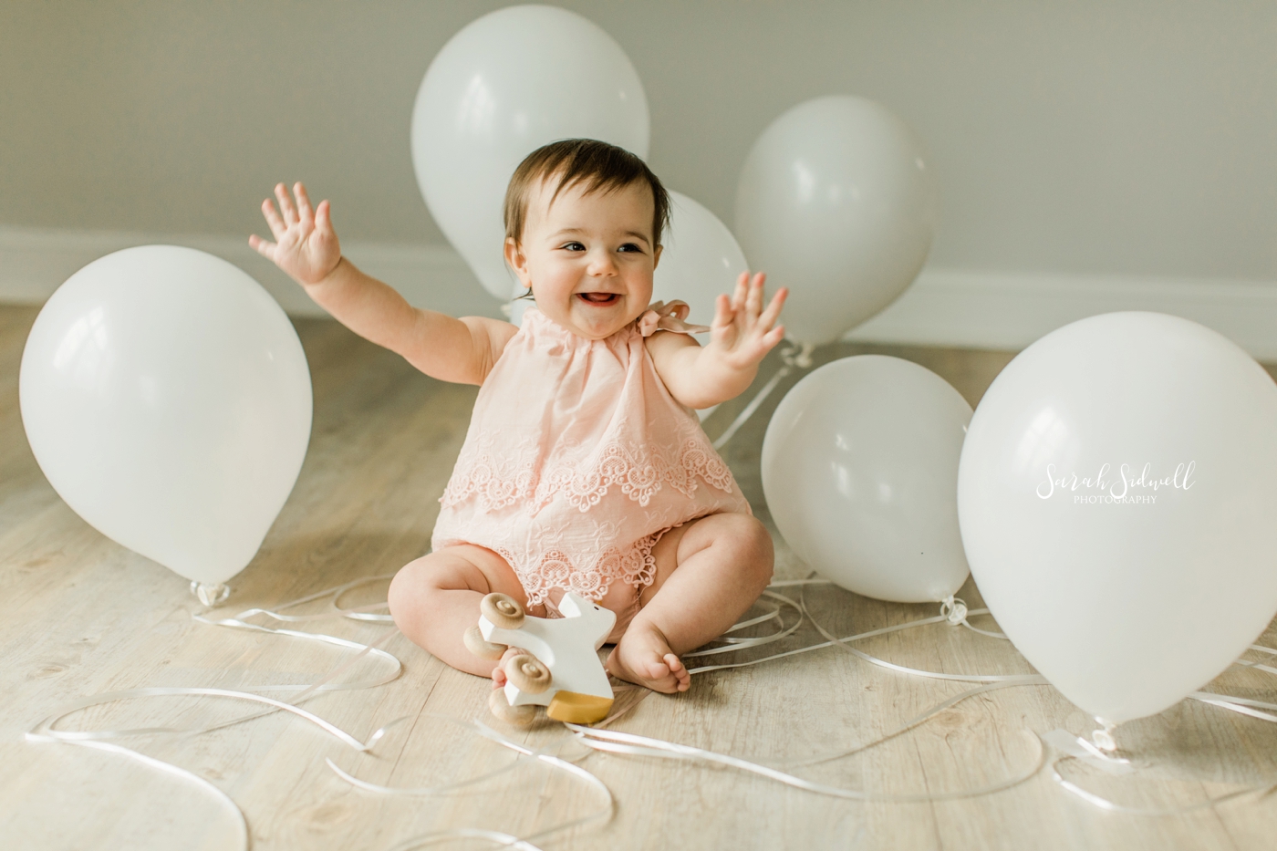 A baby sits with white balloons