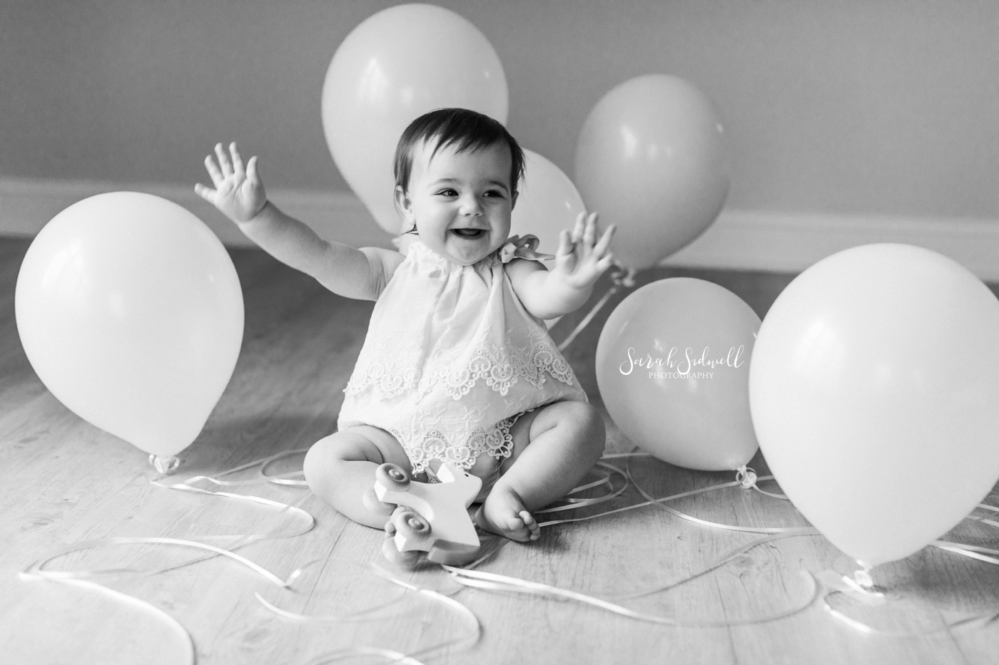 A baby pushes balloons out of her way. 