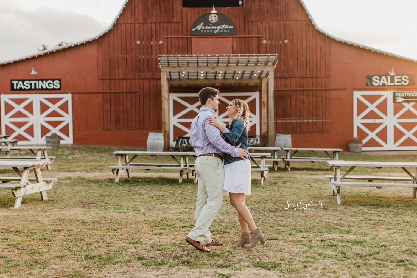 A couple kiss each other in front of a red barn. 