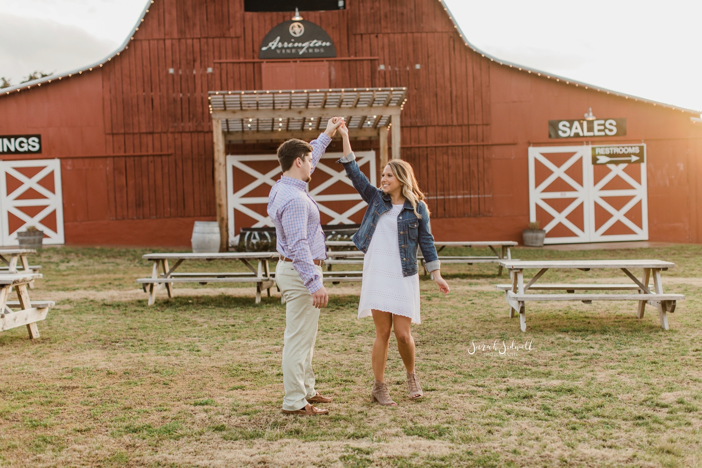 A man twirls his fiance in front of a red barn at Arrington Vineyards. 