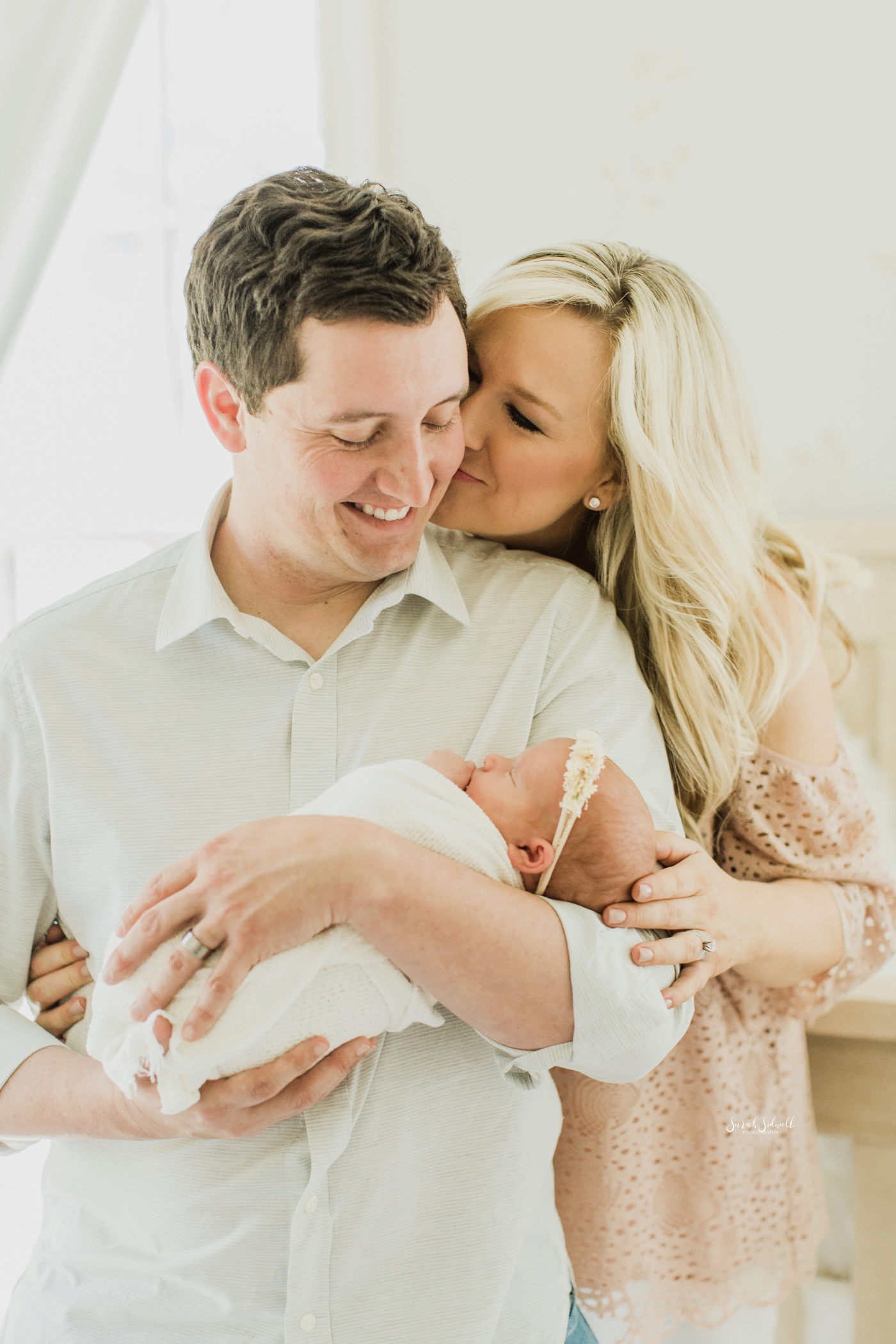 A mom kisses her husband while he holds their baby. 
