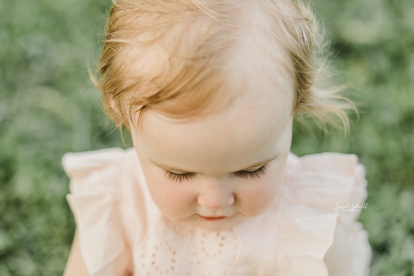 A red headed toddler looks down at her feet. 