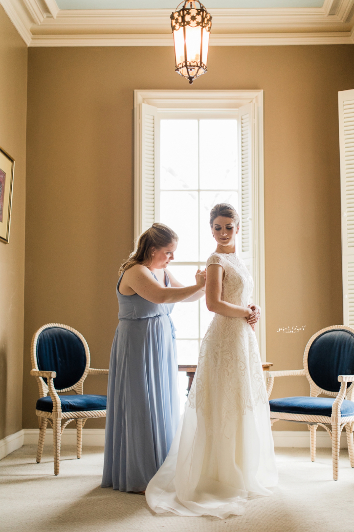 A bridesmaid helps a bride get ready. 