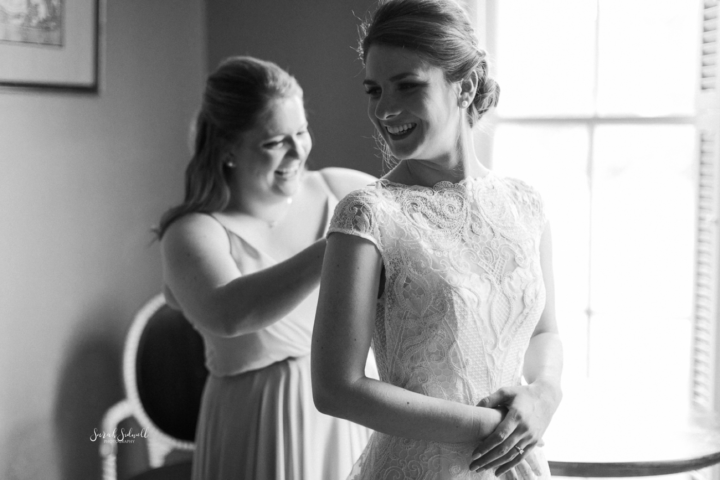 A bride's friend helps her get into her dress. 