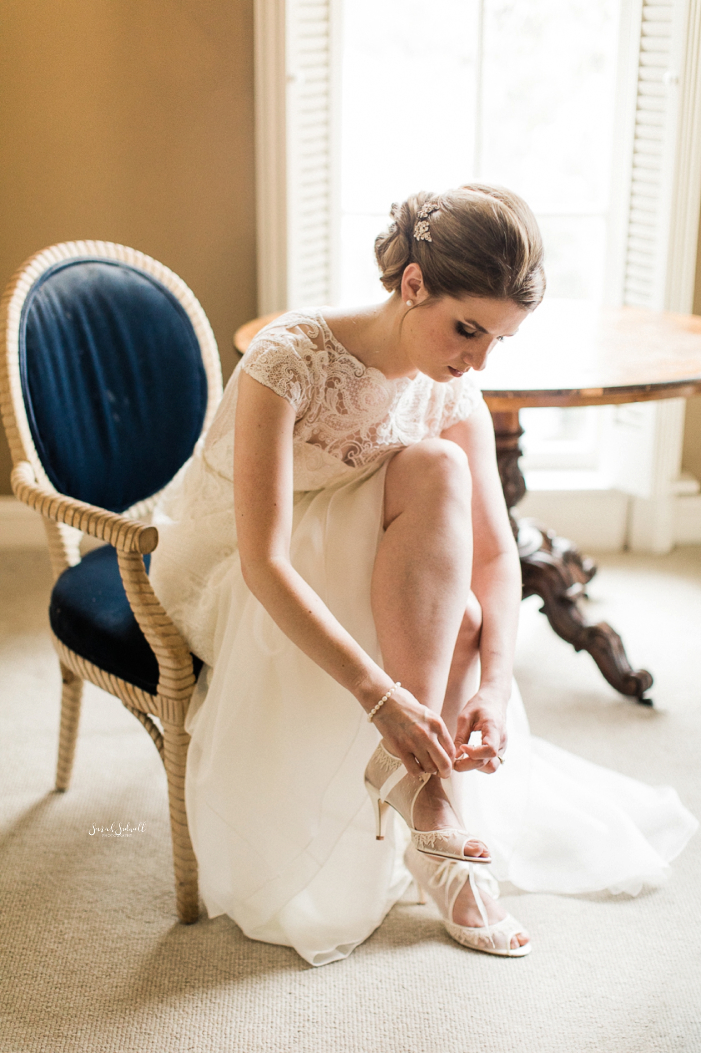 A bride sits to buckle her shoe. 