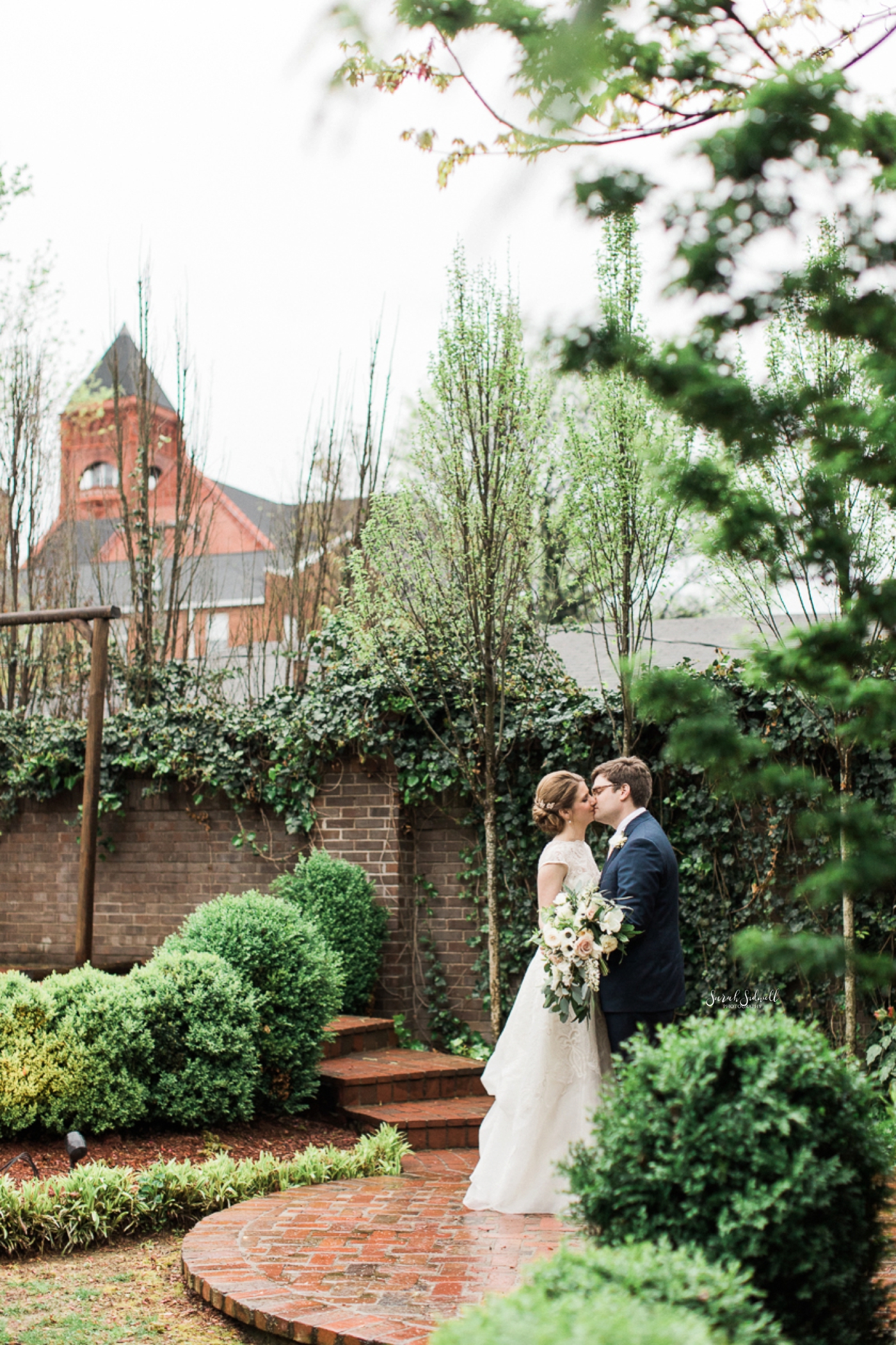 A bride and groom steal a kiss in a secret garden. 