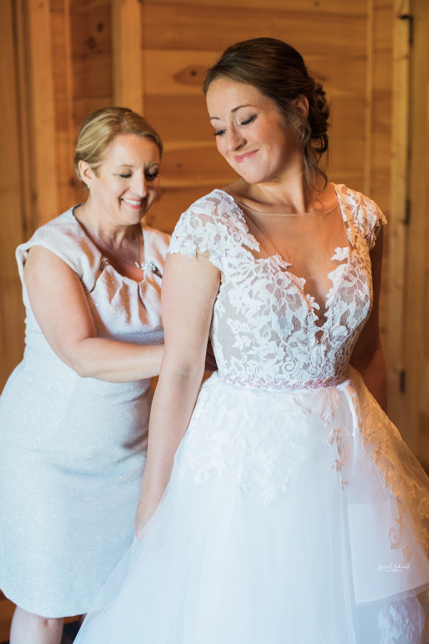 A bride gets help fastening her dress. 