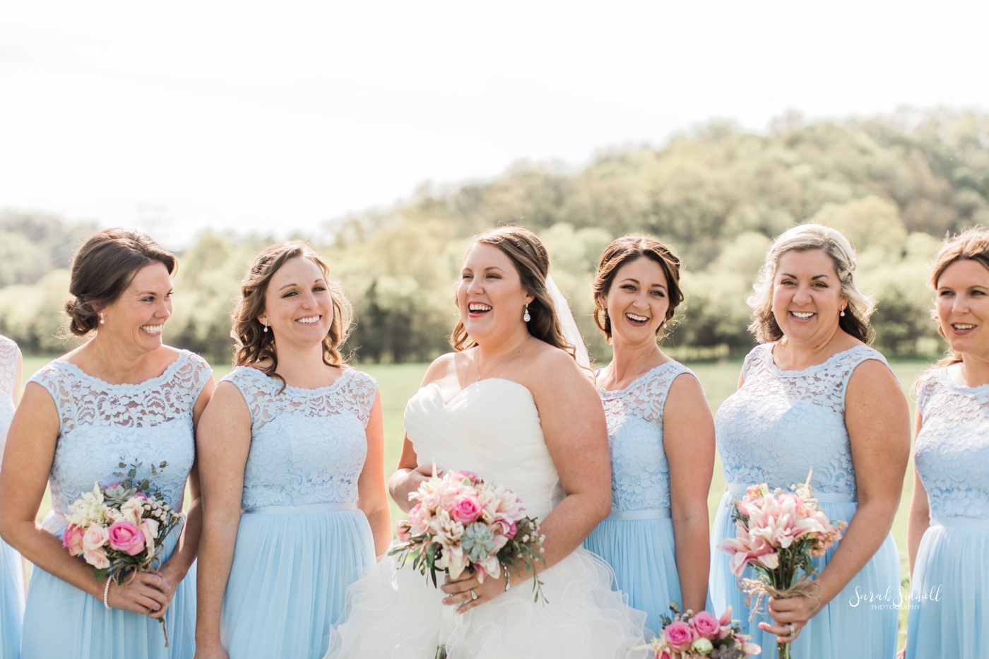 A bride stands with her bridal party who wear blue dresses. 