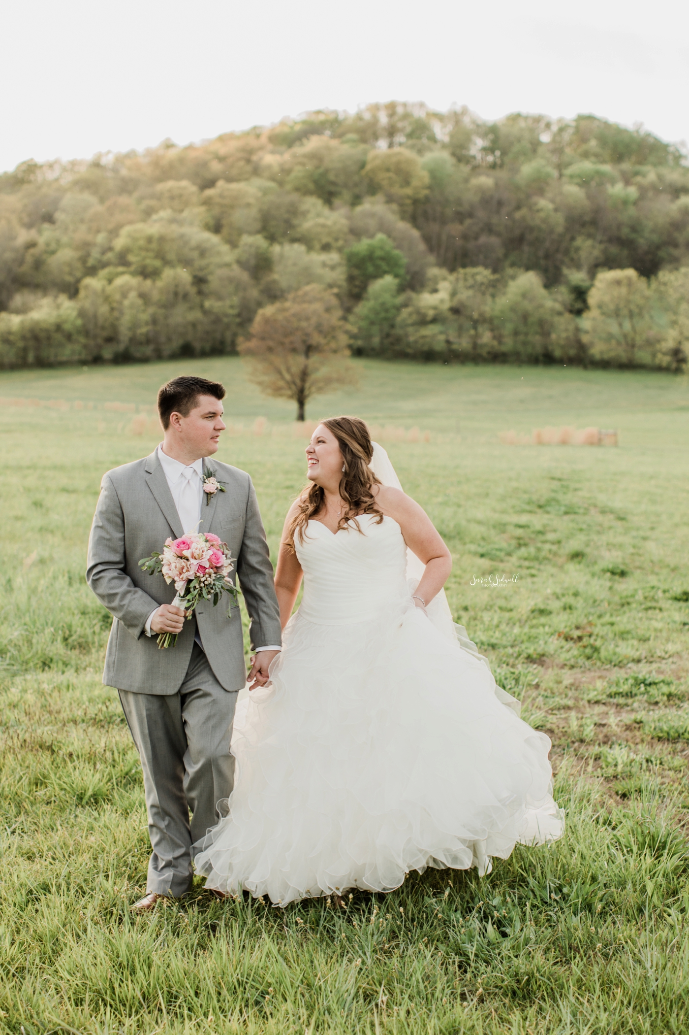 A bride and groom twirl in a green field. 