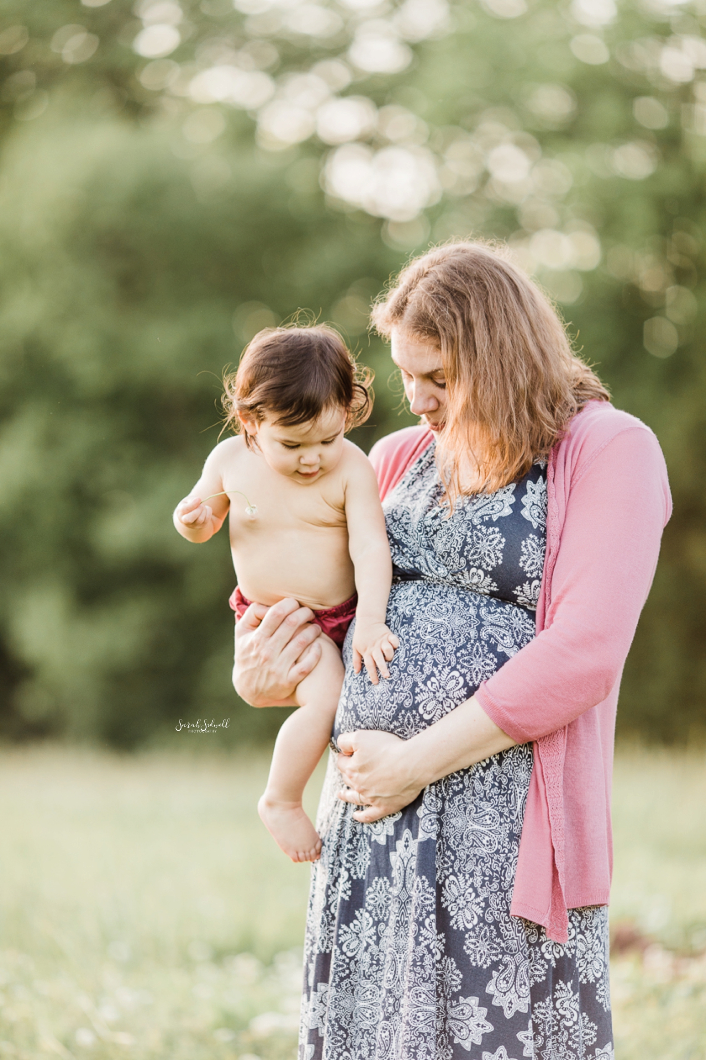A mom holds her toddler during her family maternity photography session. 