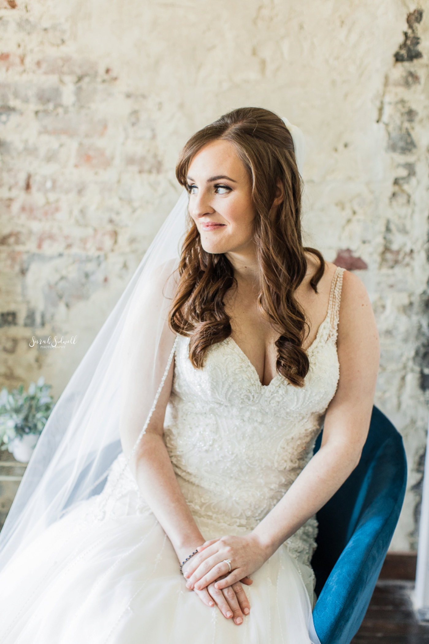 A woman sits in a chair while wearing her wedding dress. 