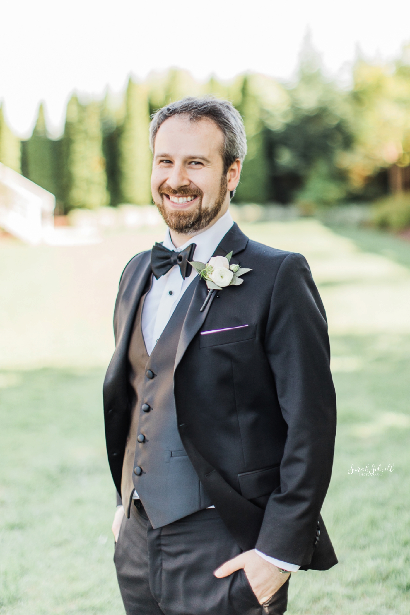 A man wears a tux for his wedding and puts his hand in his pocket. 