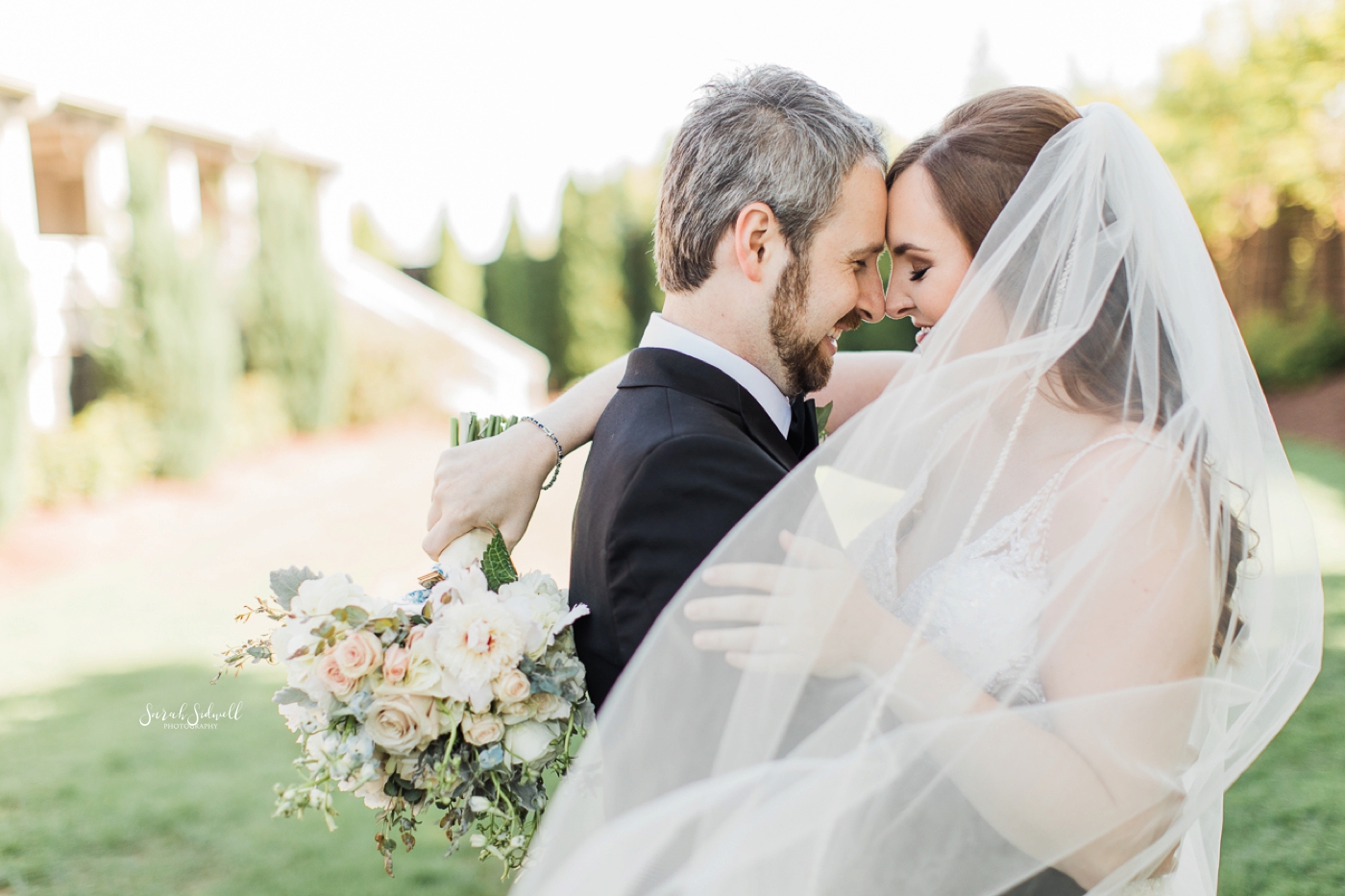 A bride hugs her groom around the neck as she holds her flowers. 