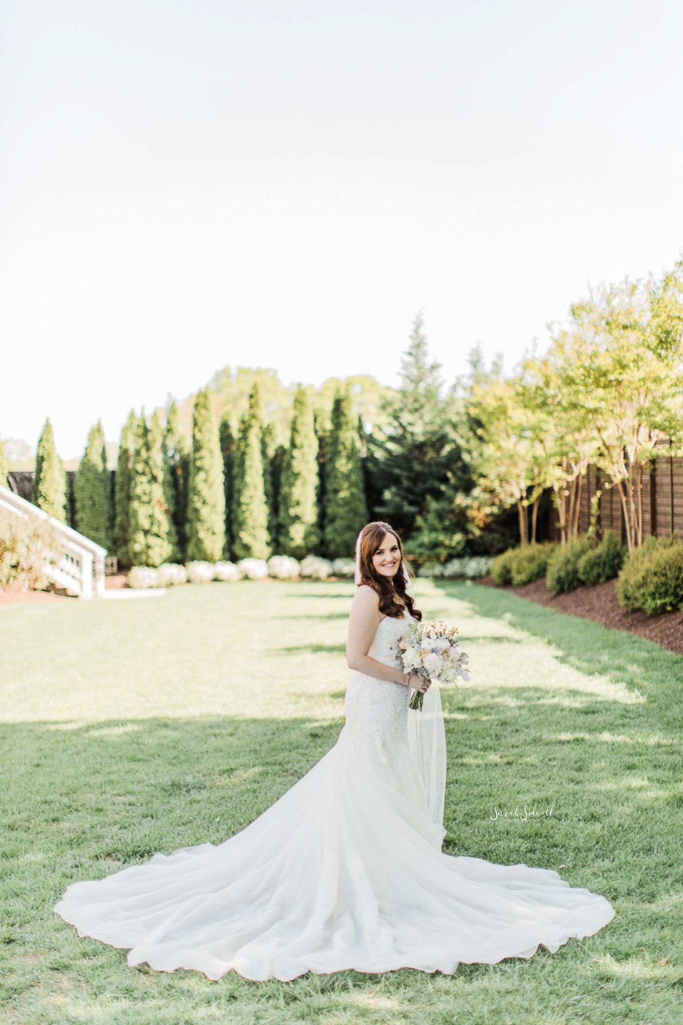 A bride stands in a green field with her dress spread out. 