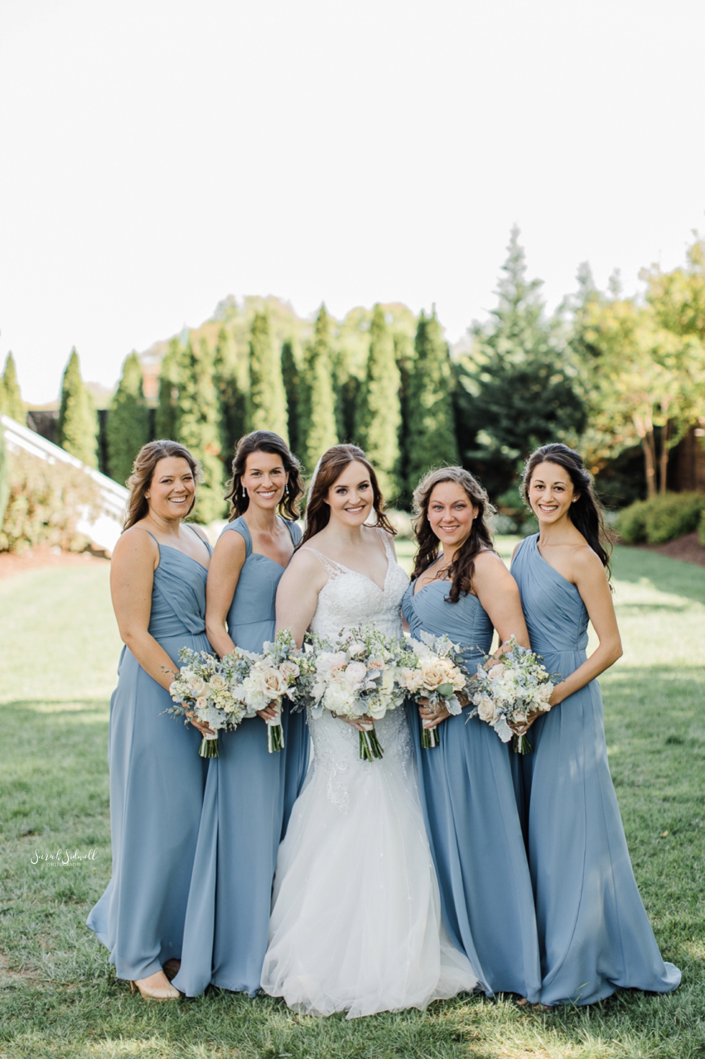 A bride stands with her bridal party and smiles. 