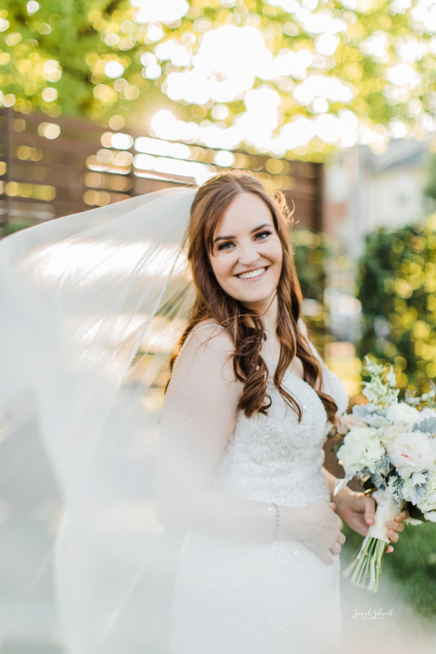 A bride's veil flows around her as she smiles. 