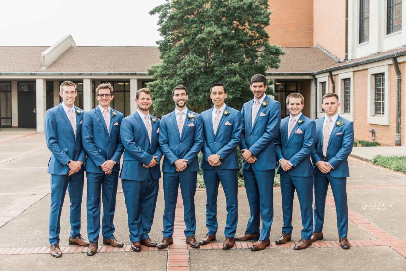 Groomsmen in blue suits stand in a line together. 
