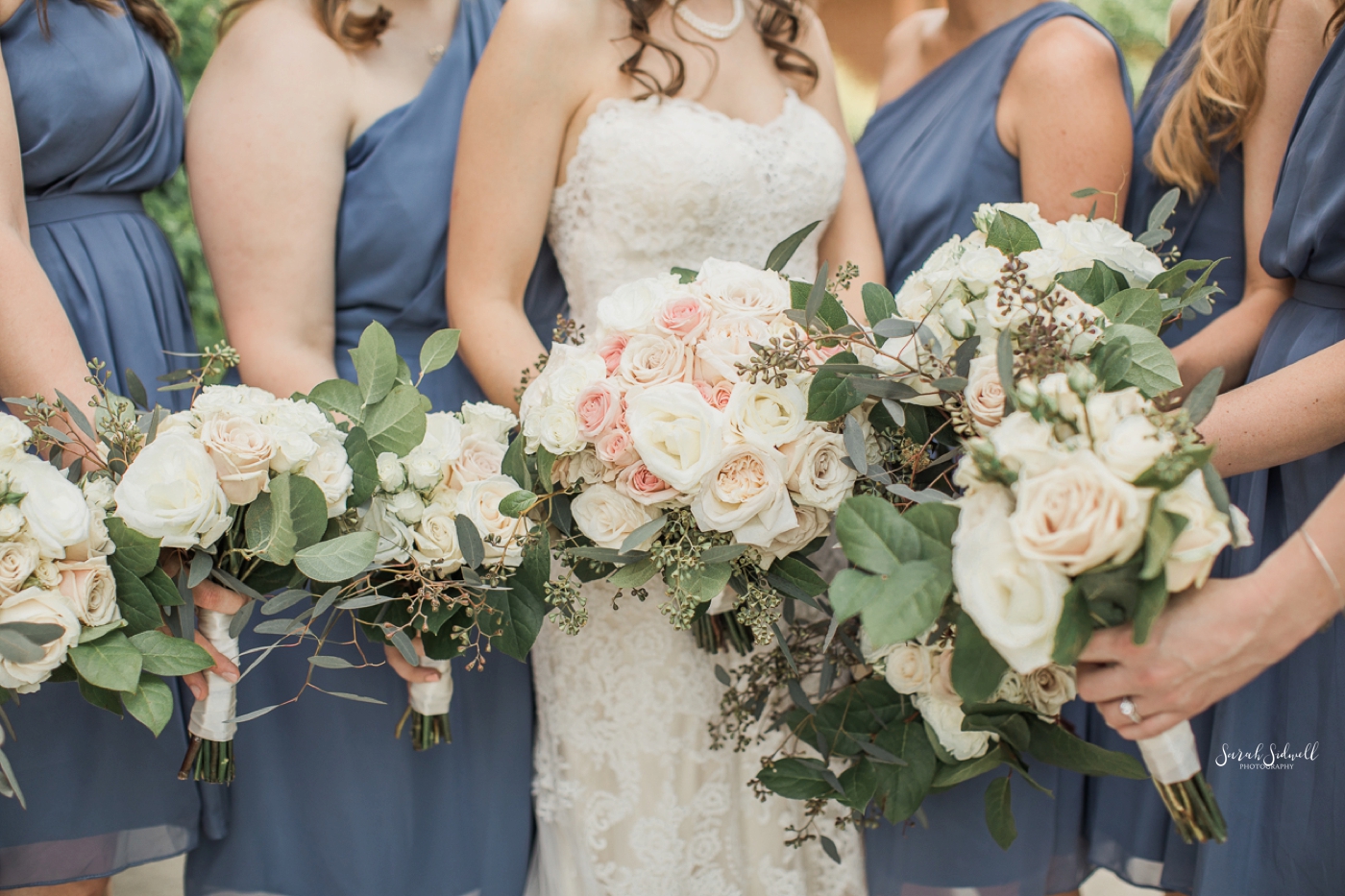 A bridal party holds out their flowers in a big bunch. 