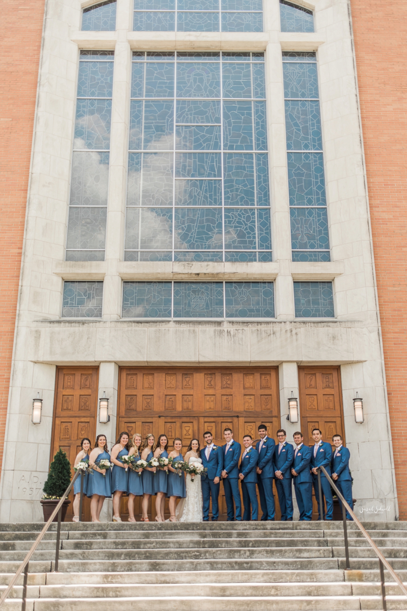 A wedding party stands in front of a tall building with tall windows. 