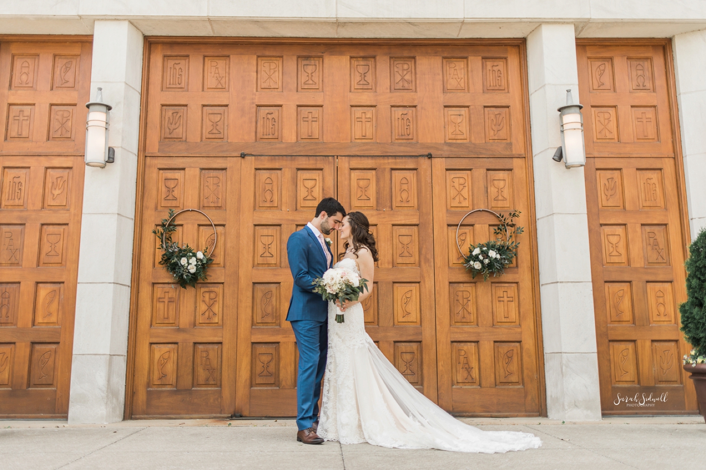 A groom kisses his bride in front of large wooden doors. 