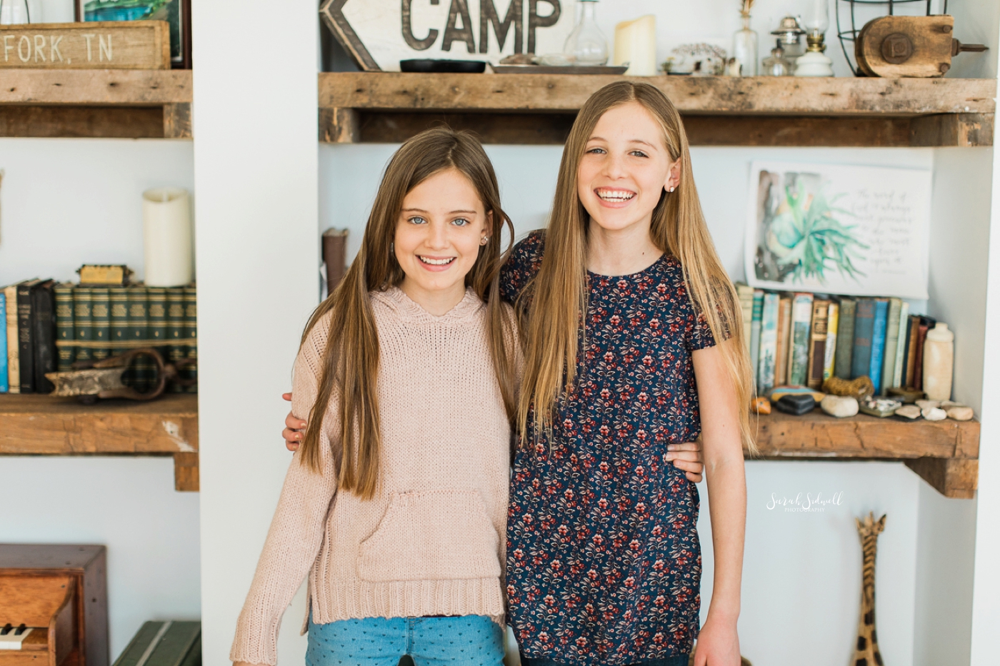 Two teen sisters stand side-by-side and smile. 