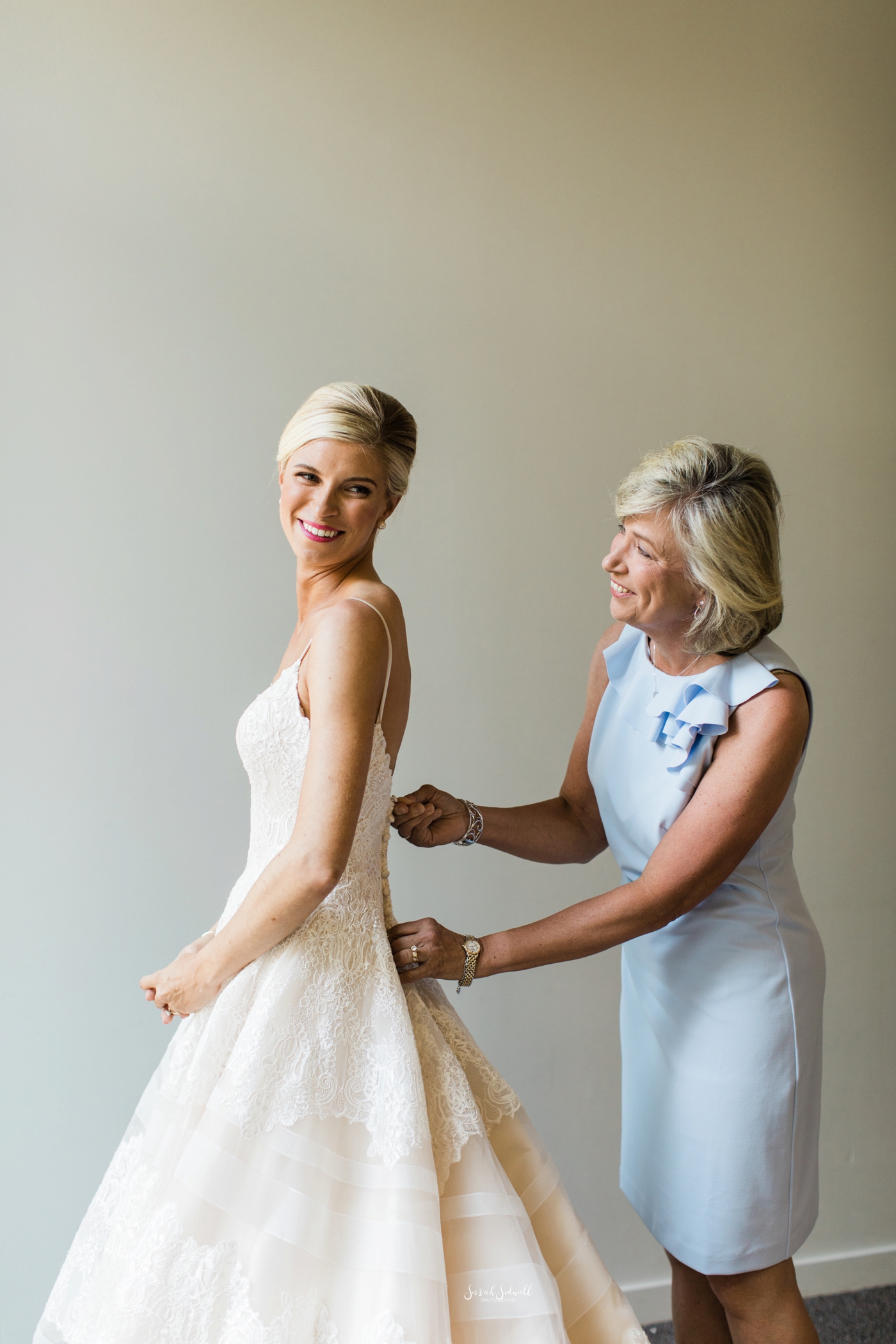 A bride's mother helps her to get into her wedding dress. 