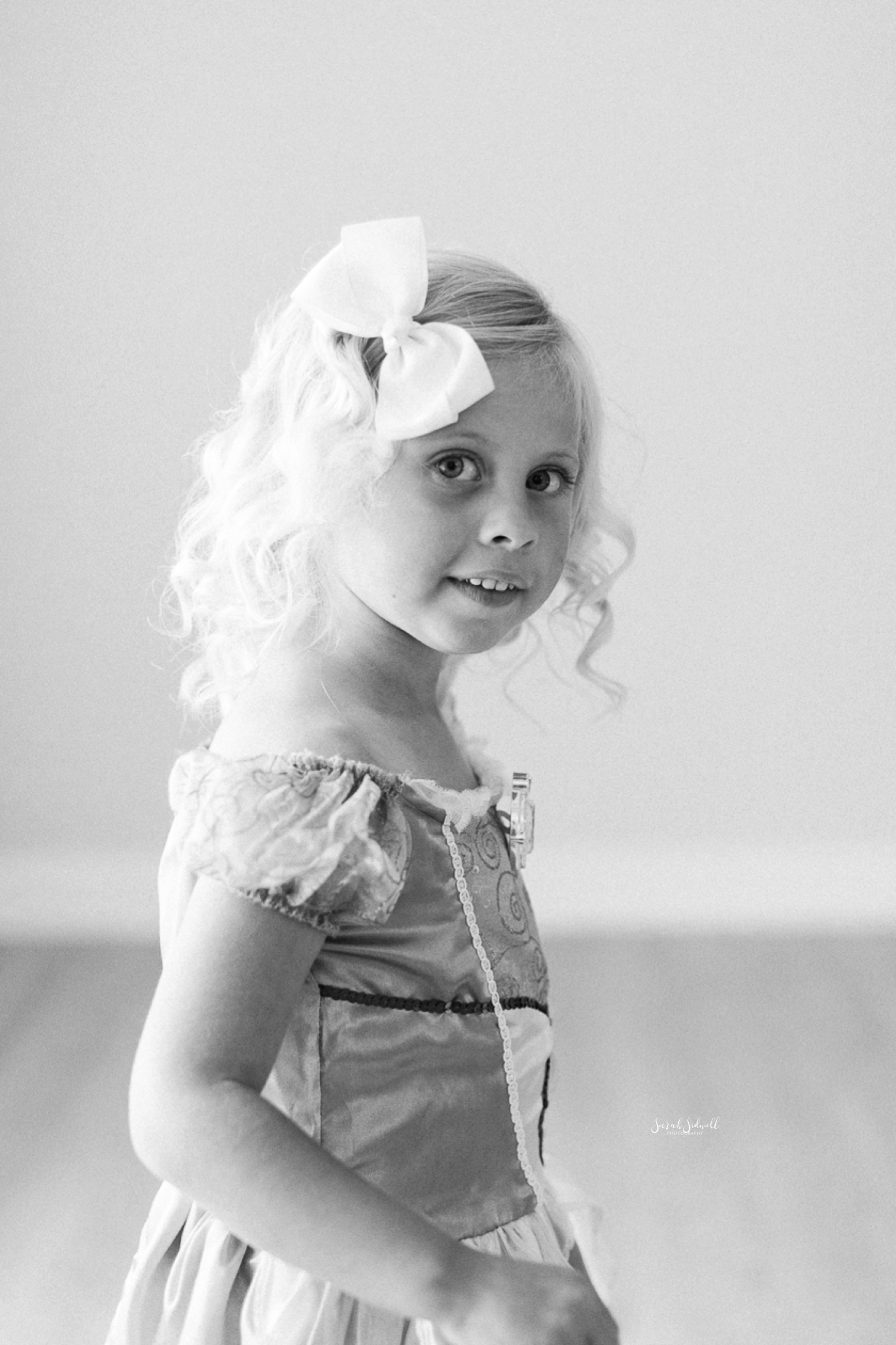 A little girl wears a white bow in her hair. 