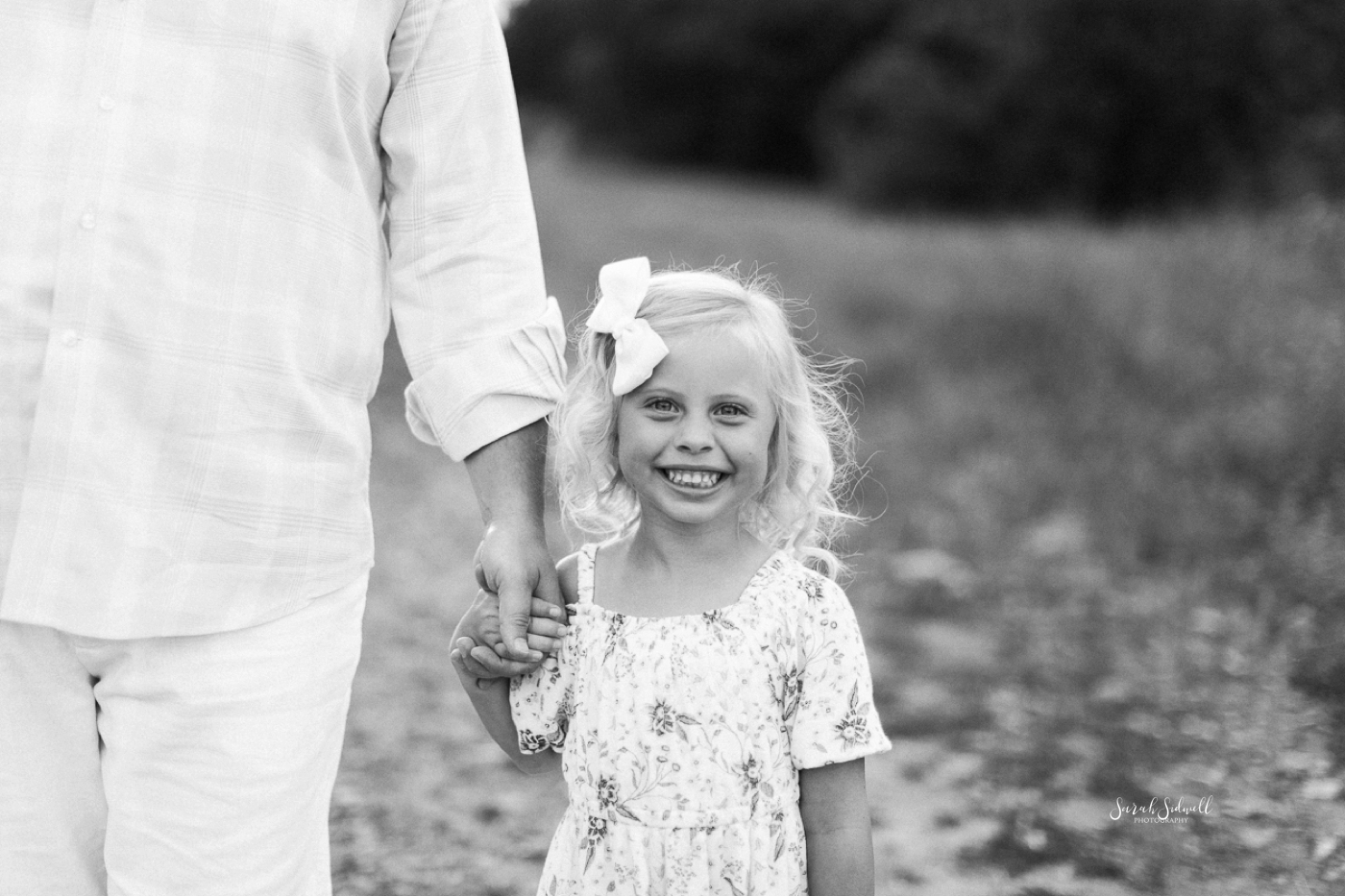 A girl smiles big as she holds her daddy's hand. 