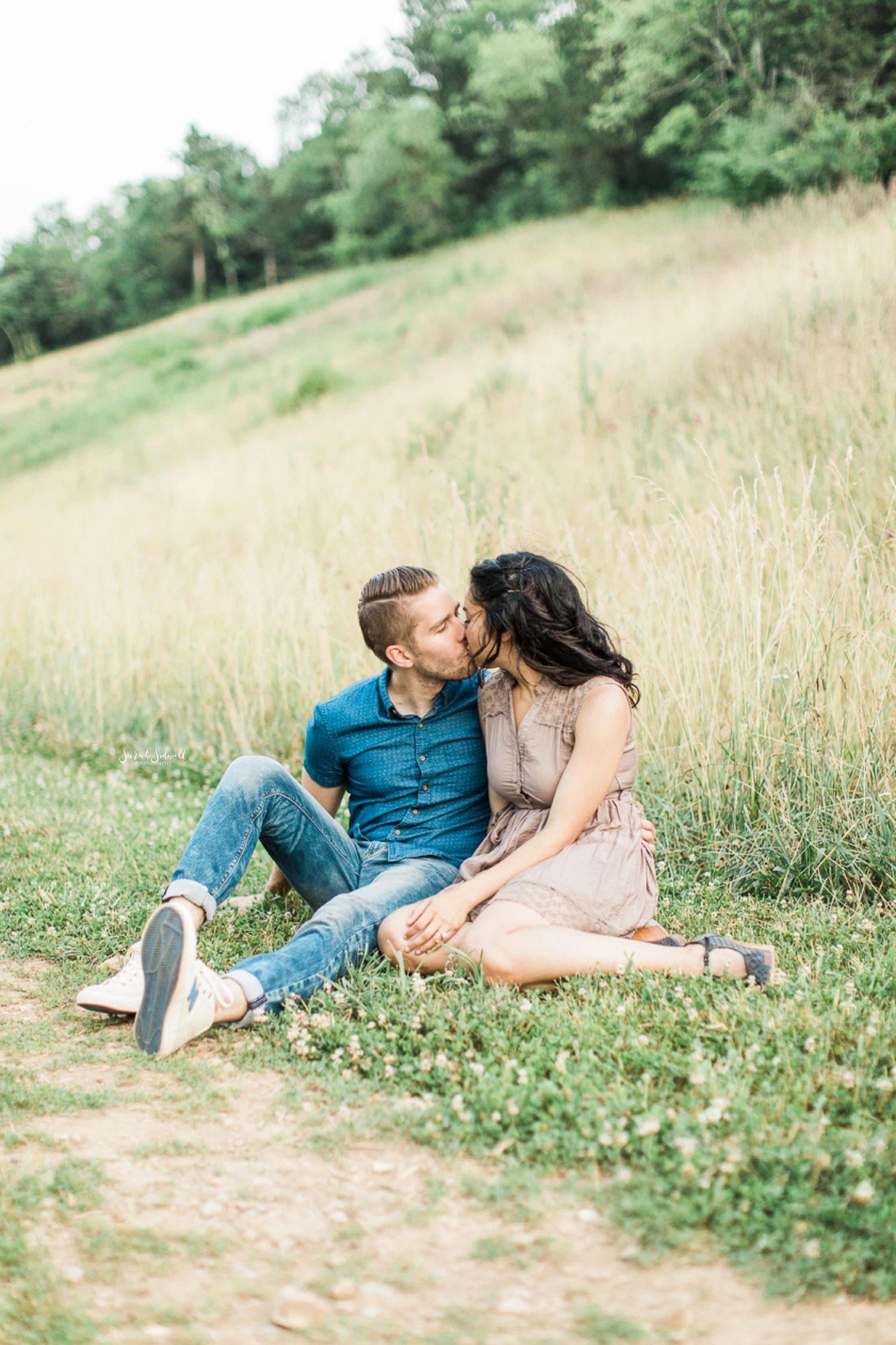 A couple sit together in some green grass to share an intimate moment. 