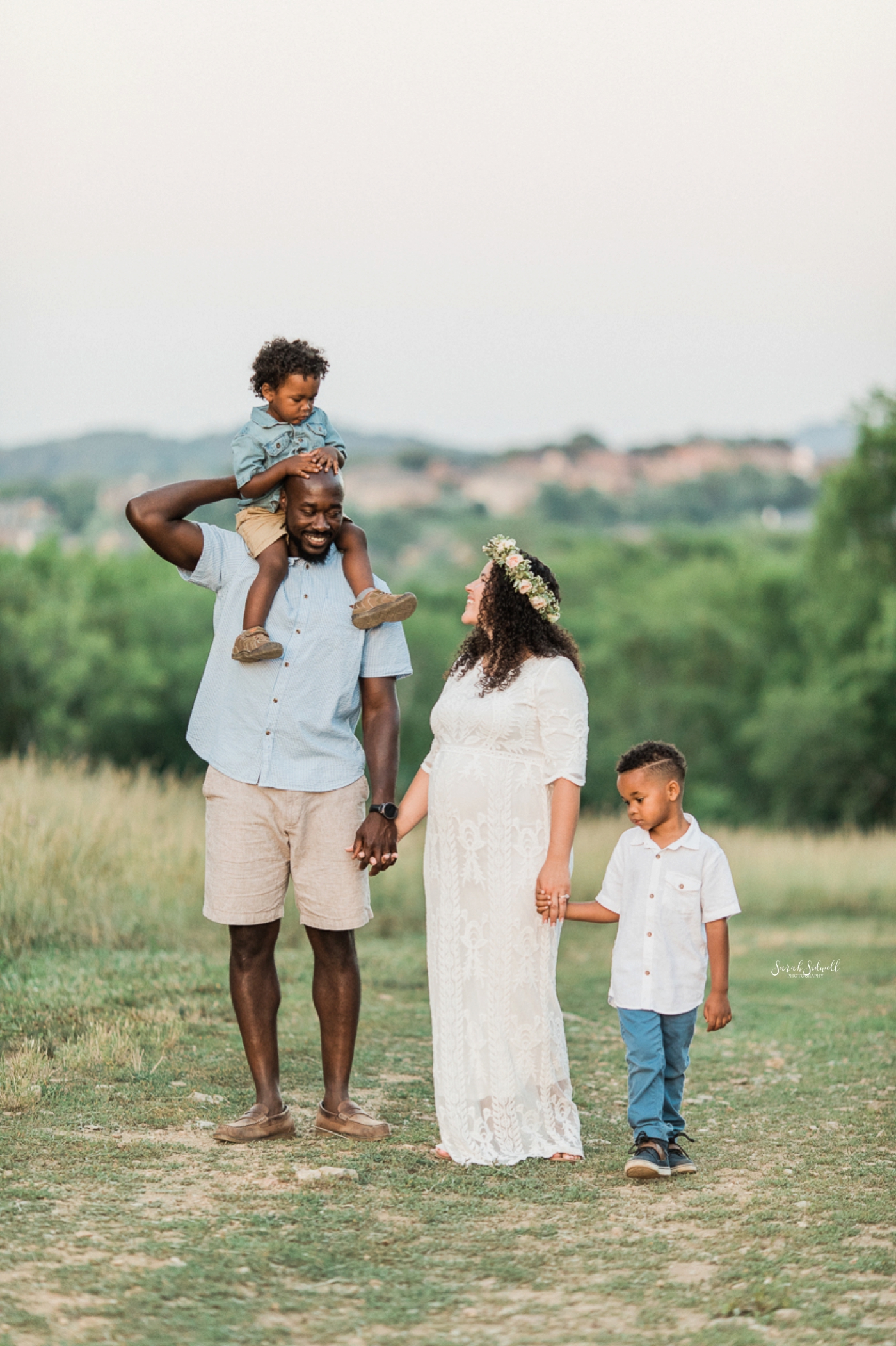 A family stand in a field of fresh green grass for their family maternity session. 