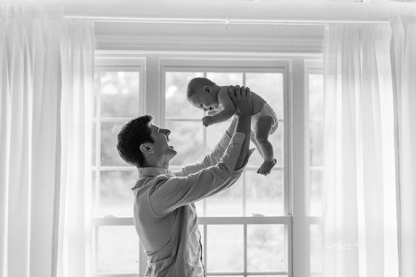 A father holds his baby in the air. 