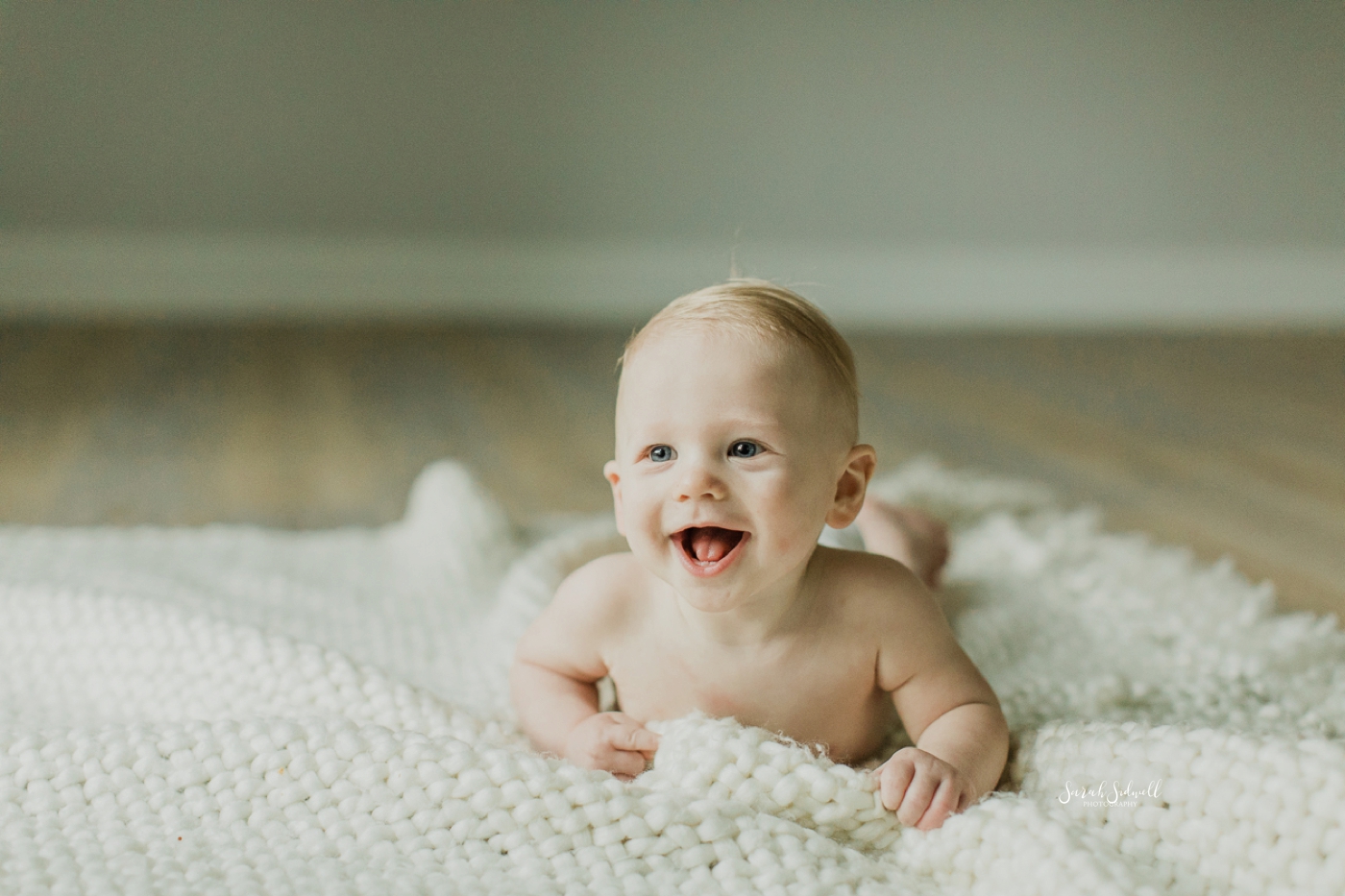 A baby laughs while laying on his tummy. 