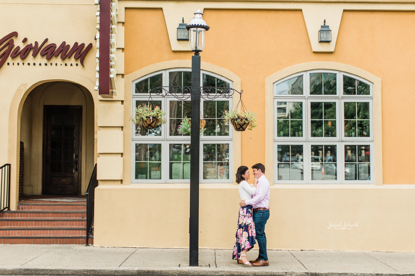 A couple embrace in front of a yellow building. 