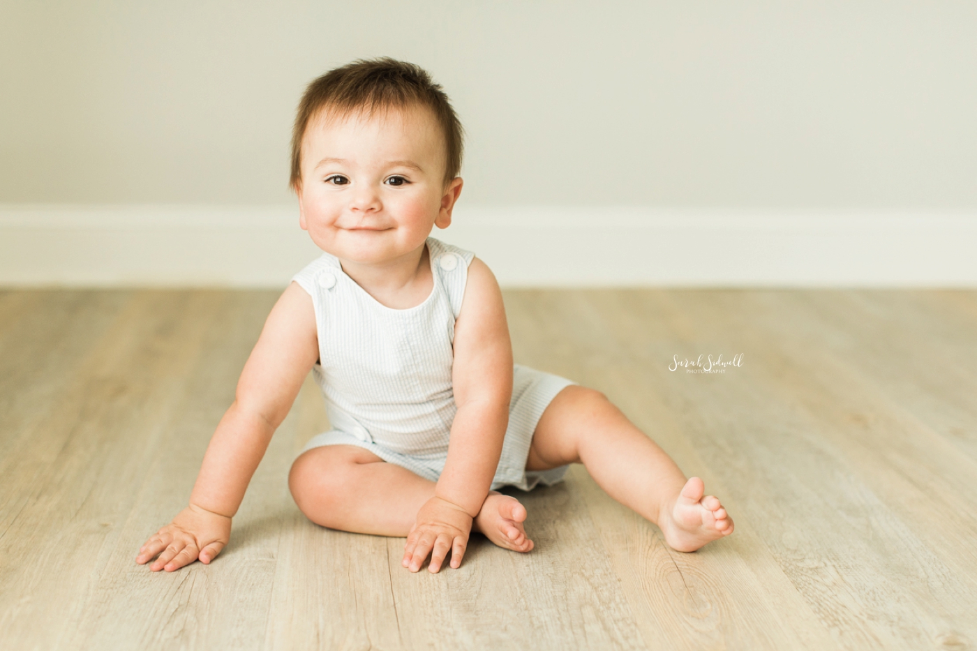 A baby sits up on a wooden floor. 