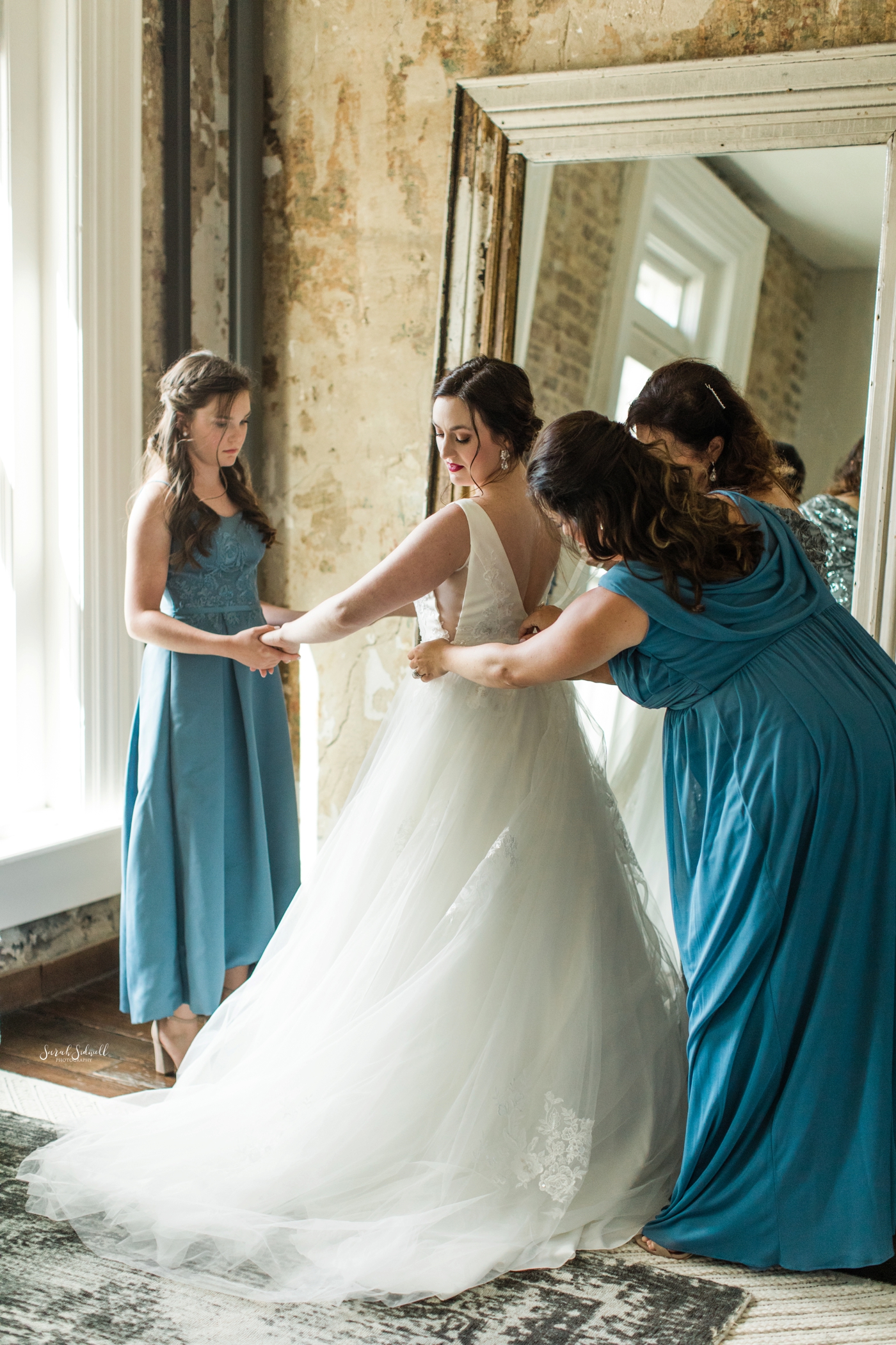 A bridesmaid zips up the bride's dress. 