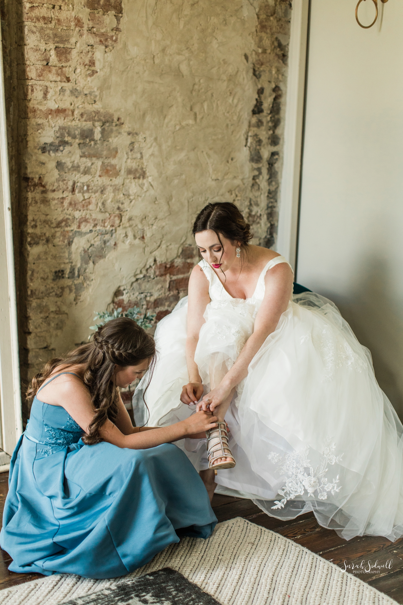 A bride gets some help putting on her shoes. 