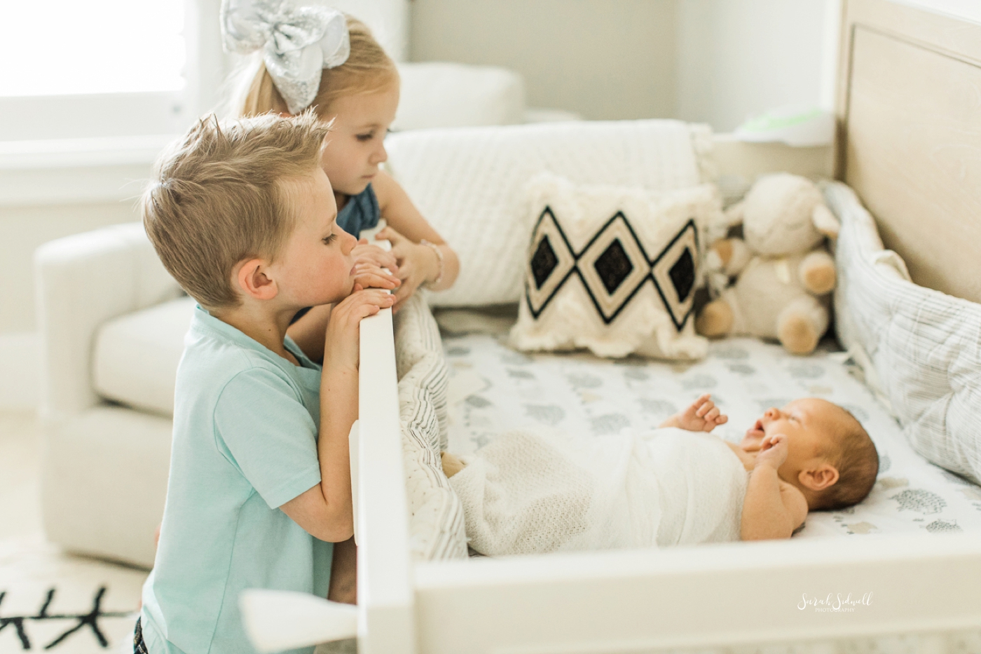 Two siblings look down at their new baby brother. 