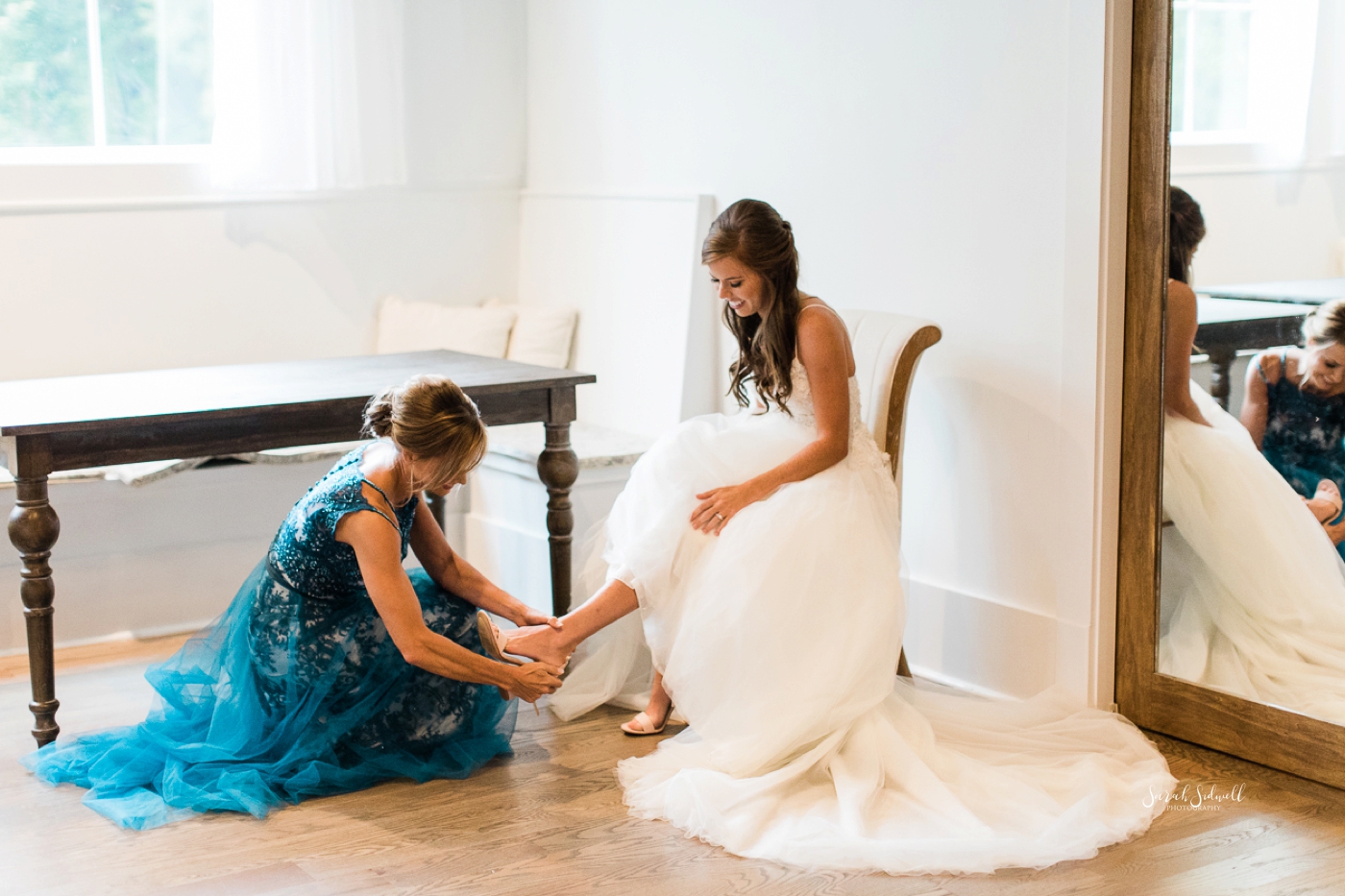 A bridesmaid helps put on a bride's shoe. 